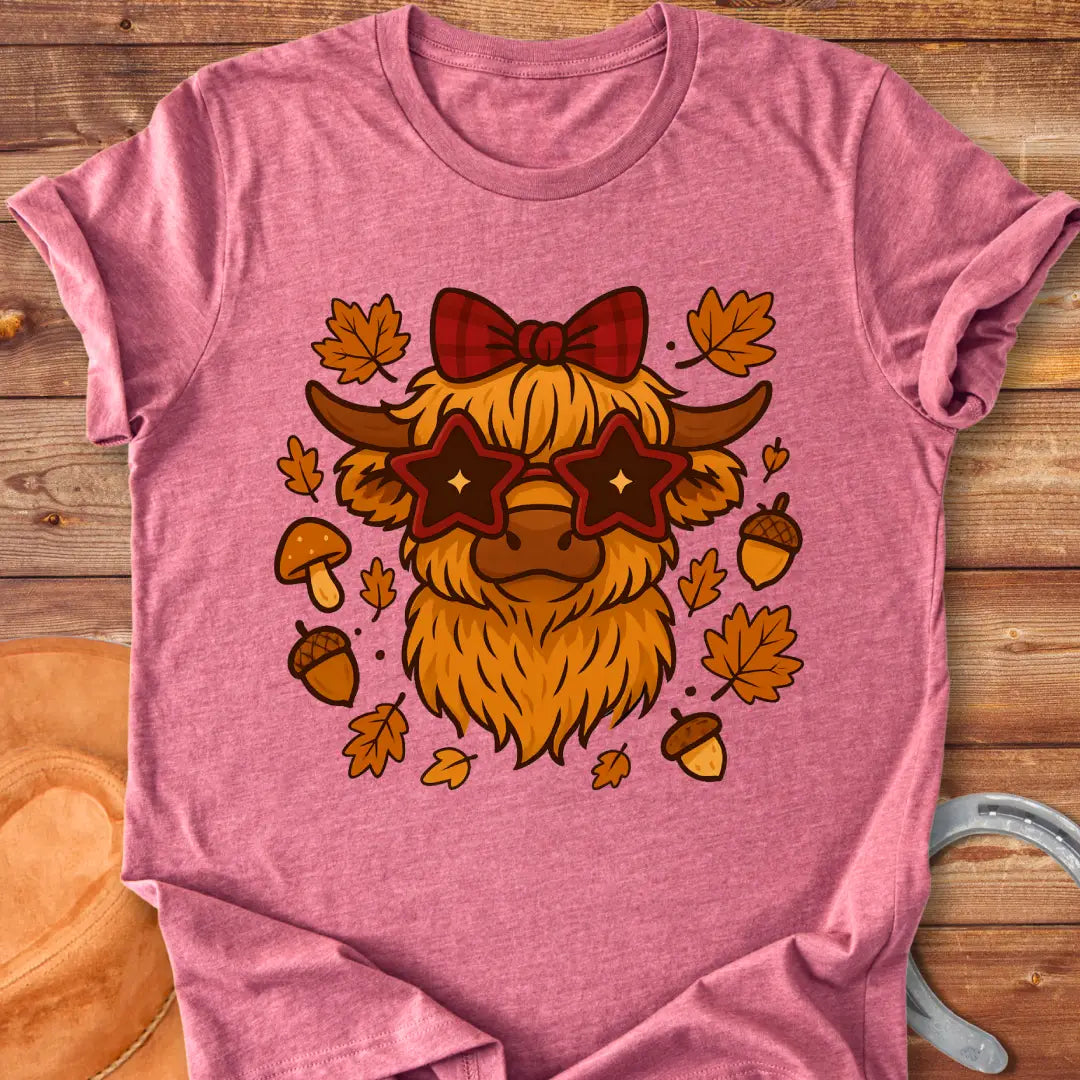 Cartoon illustration of a Highland cow wearing star-shaped sunglasses and a bow, surrounded by acorns, mushrooms, and fall leaves.