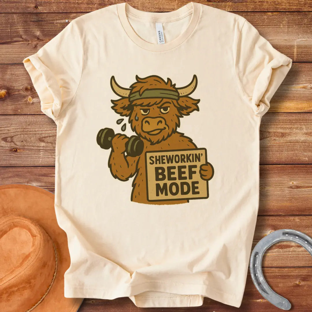 Cartoon cow working out with dumbbells, wearing a headband and holding a sign that says 'Sheworkin' Beef Mode'