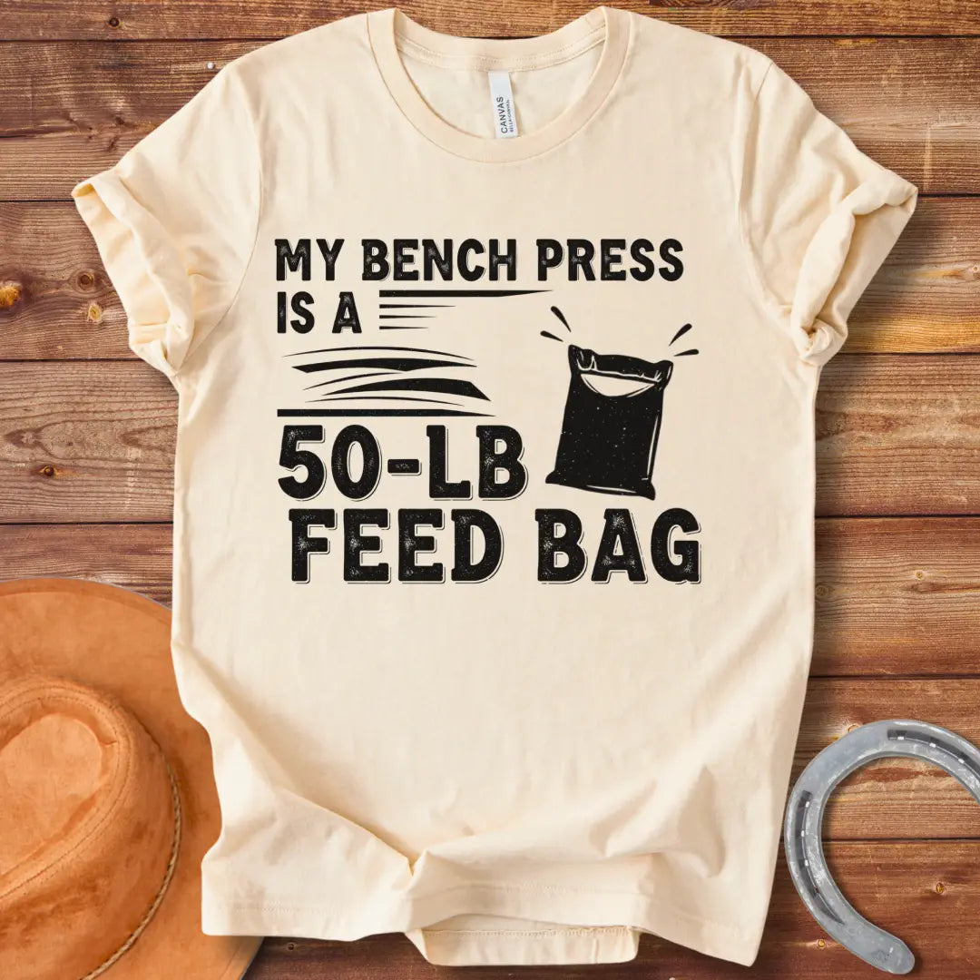 A graphic design on a t-shirt showing a humorous depiction of a feed bag labeled as a '50-lb' weight for a bench press.