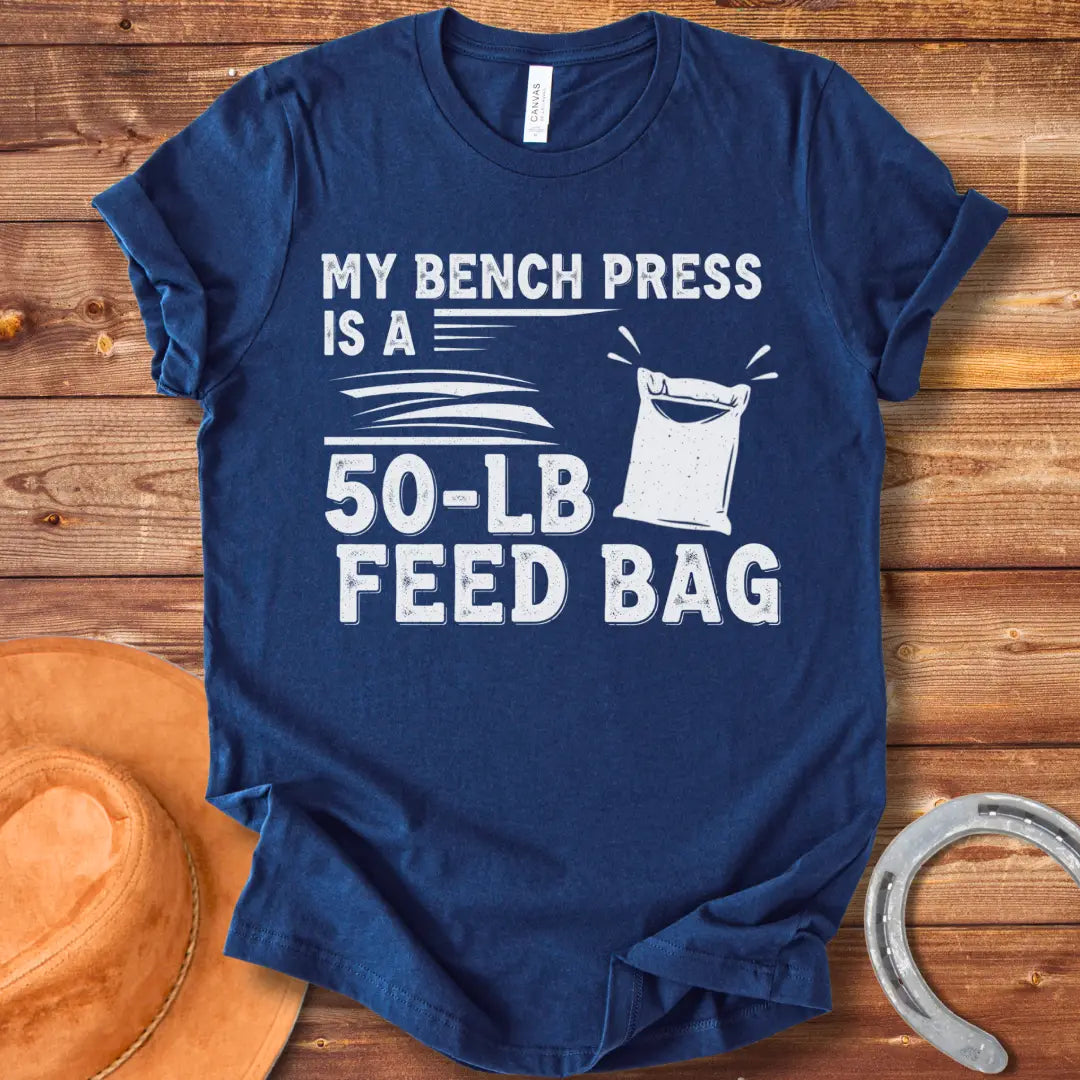 A graphic design on a t-shirt showing a humorous depiction of a feed bag labeled as a '50-lb' weight for a bench press.