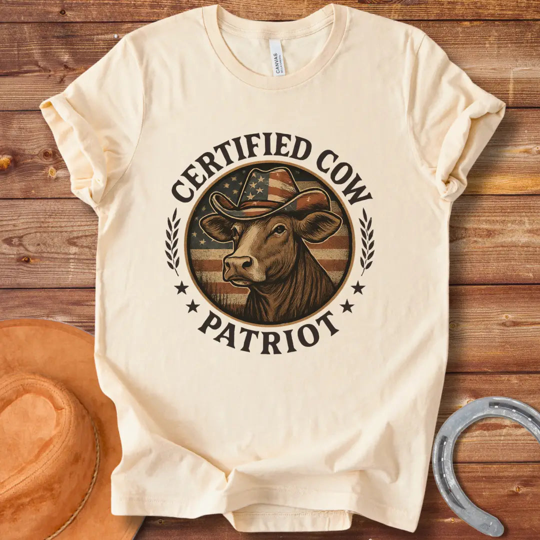 Certified Cow Patriot T-Shirt featuring a cow wearing an American flag cowboy hat, surrounded by stars and wheat stalks.