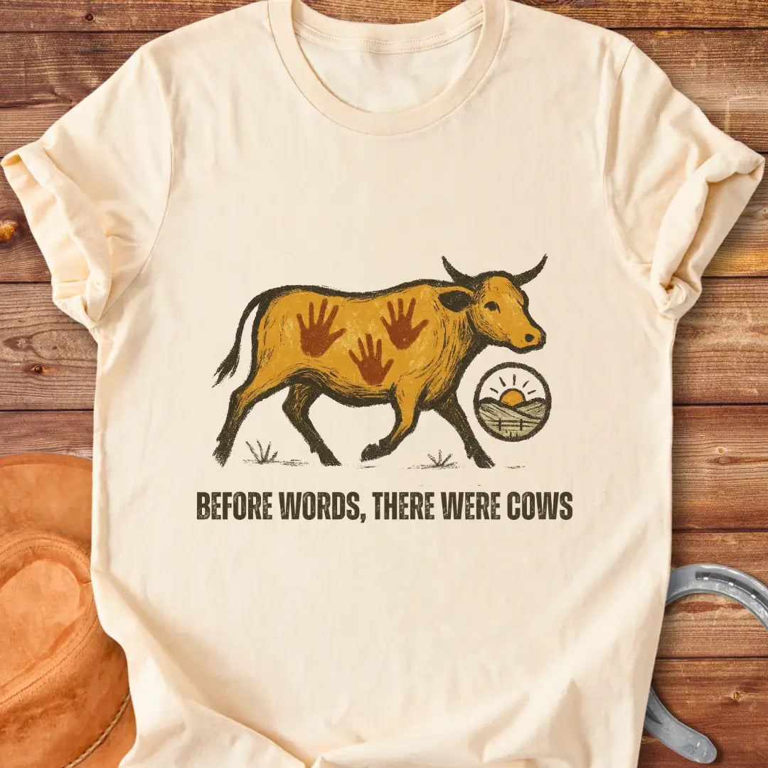 Vintage-style t-shirt design featuring a cow with handprints and the words "Before Words, There Were Cows."