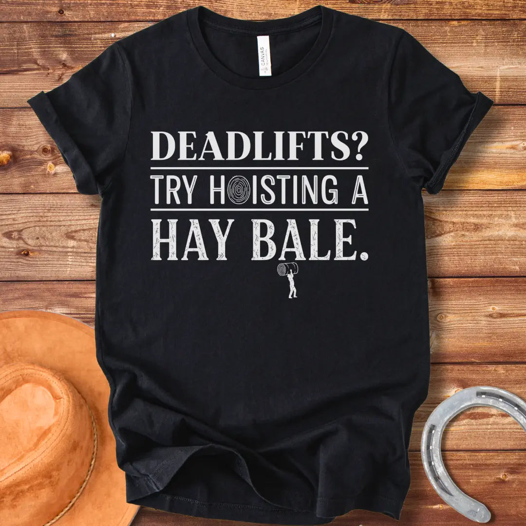 Black and white distressed text graphic on a black t-shirt that reads: 'Deadlifts? Try hoisting a Hay Bale!' with a small barbell graphic at the bottom.