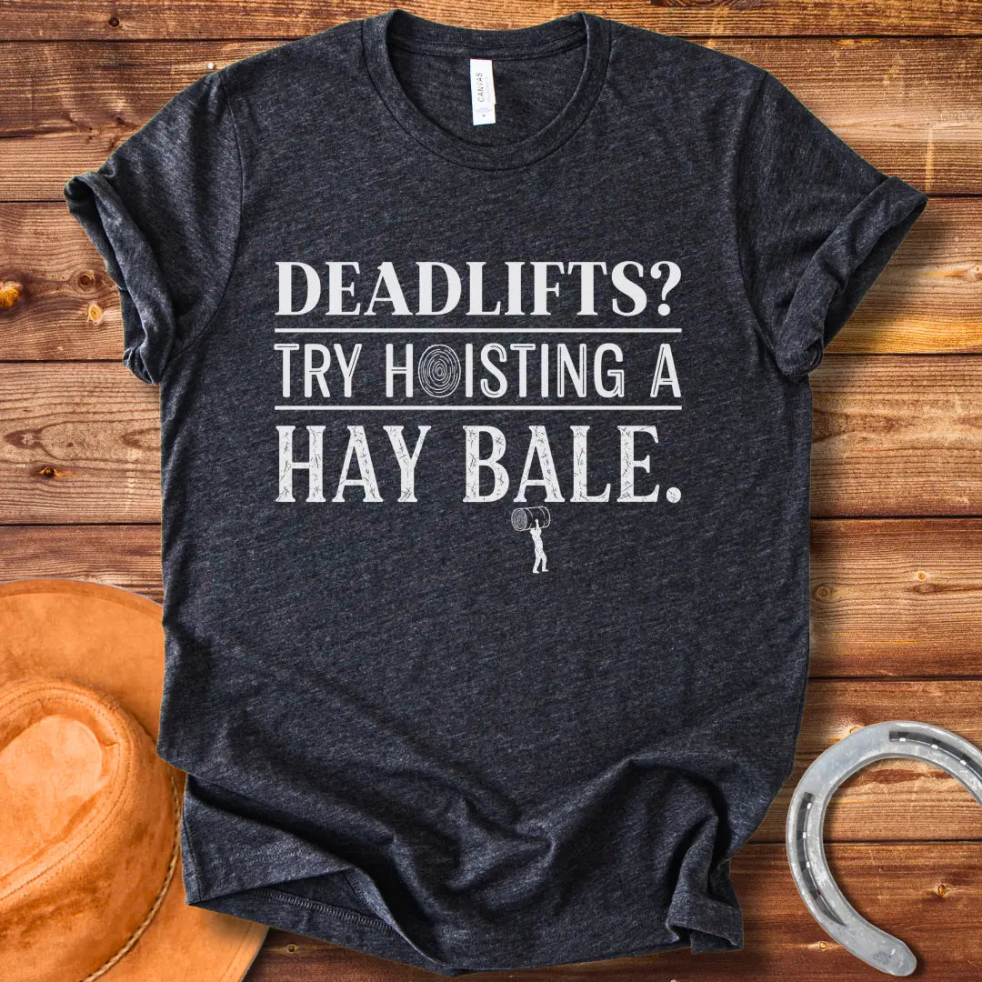 Black and white distressed text graphic on a black t-shirt that reads: 'Deadlifts? Try hoisting a Hay Bale!' with a small barbell graphic at the bottom.