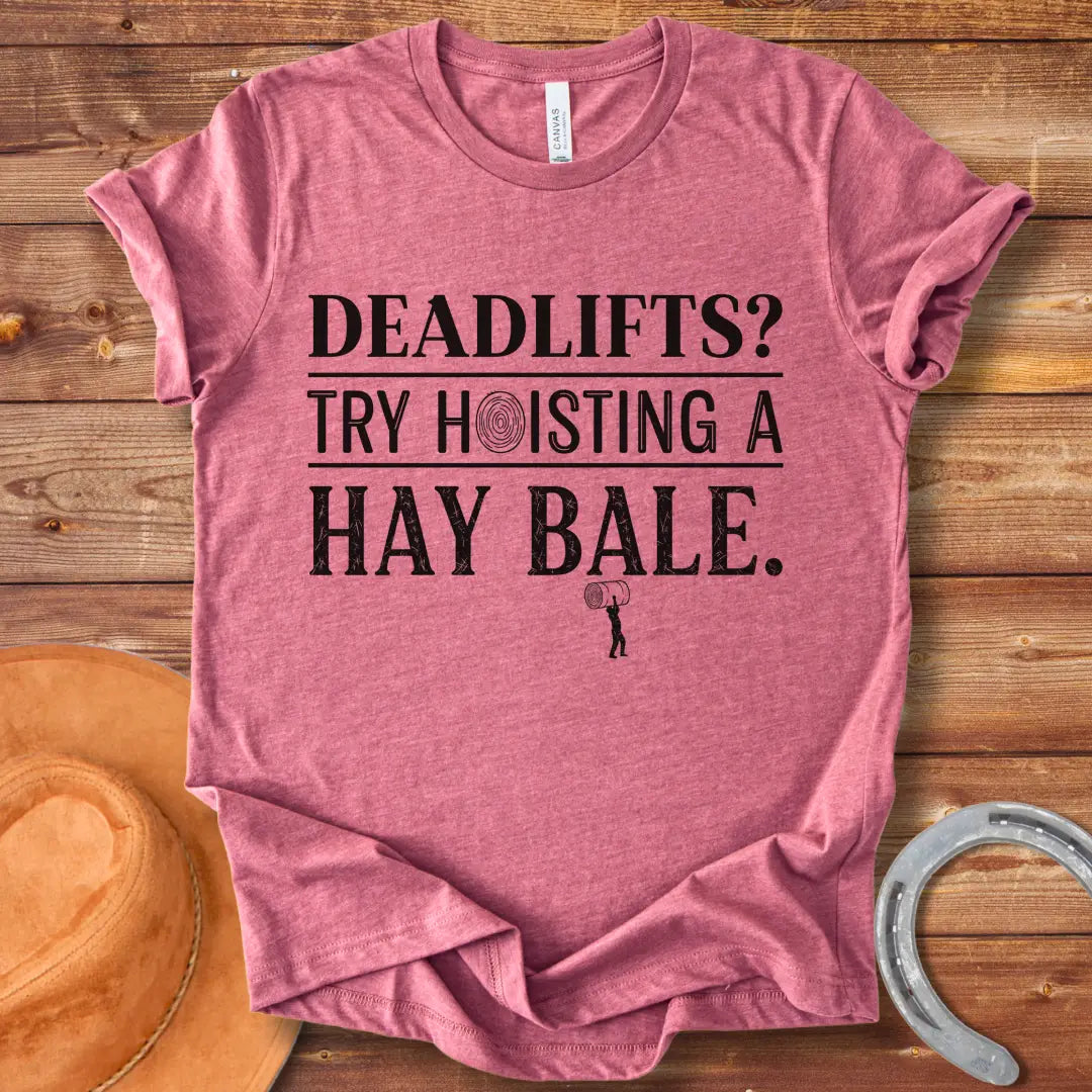 Black and white distressed text graphic on a black t-shirt that reads: 'Deadlifts? Try hoisting a Hay Bale!' with a small barbell graphic at the bottom.