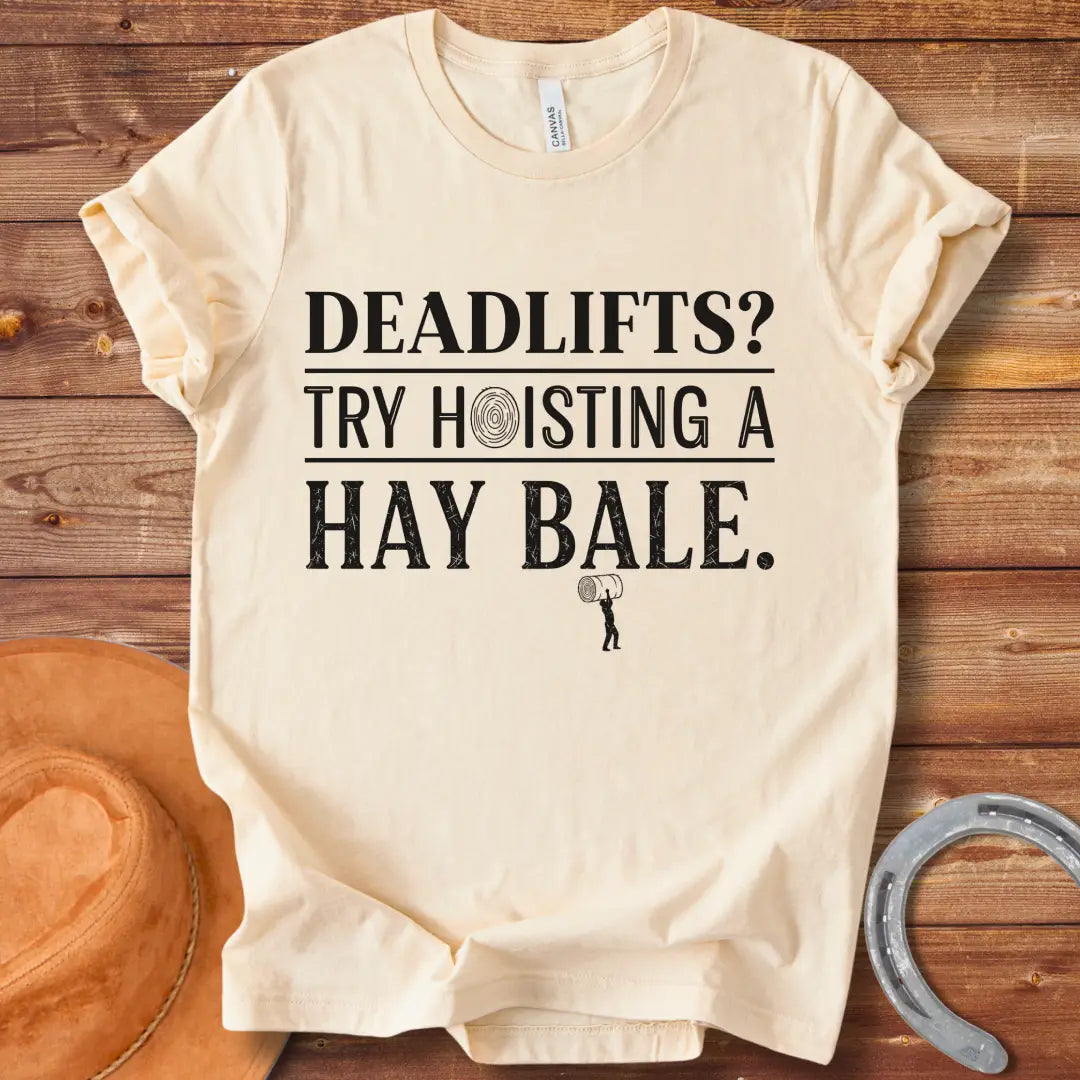Black and white distressed text graphic on a black t-shirt that reads: 'Deadlifts? Try hoisting a Hay Bale!' with a small barbell graphic at the bottom.