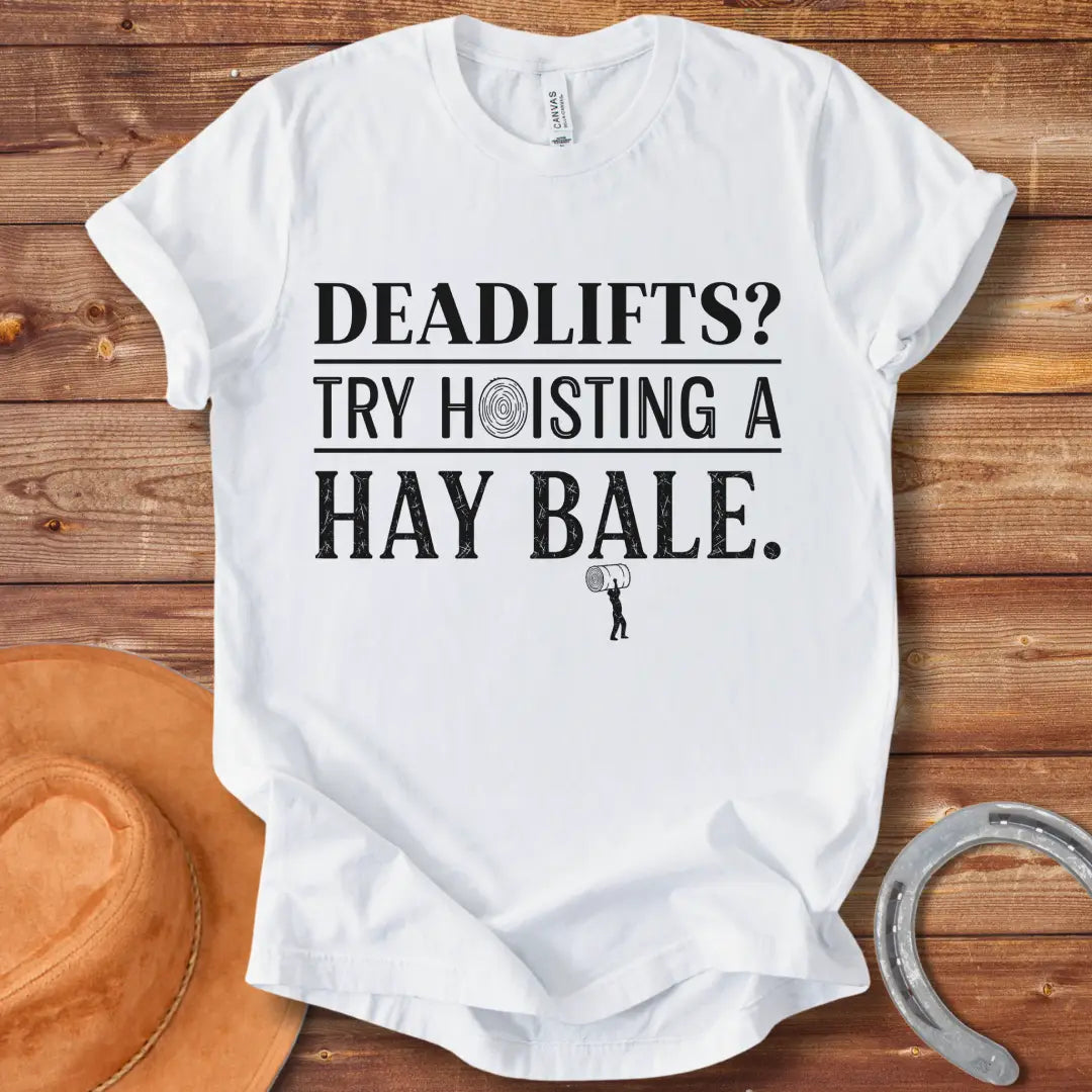 Black and white distressed text graphic on a black t-shirt that reads: 'Deadlifts? Try hoisting a Hay Bale!' with a small barbell graphic at the bottom.