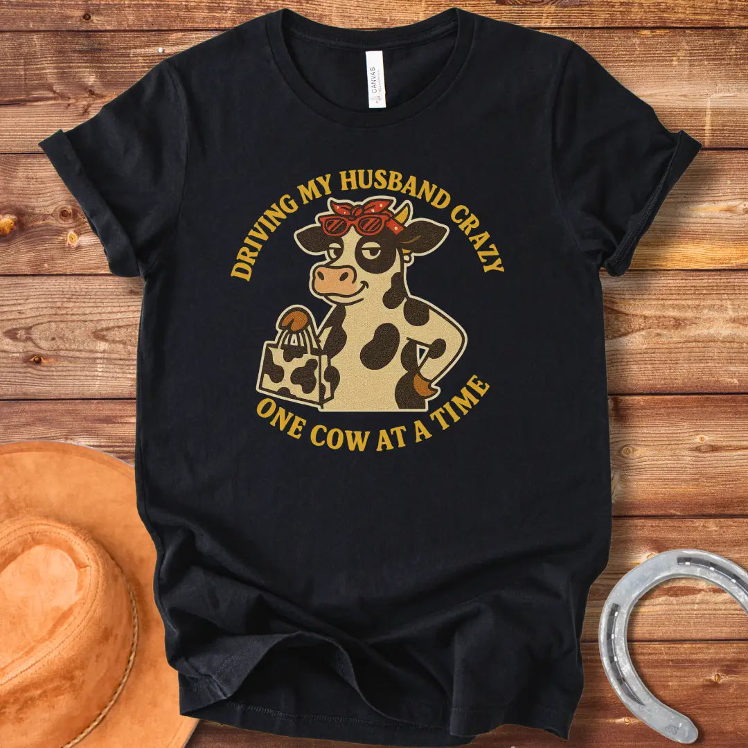 A cartoon cow wearing sunglasses and a bandana, holding a shopping bag, with the text 'Driving My Husband Crazy One Cow At A Time' around it.