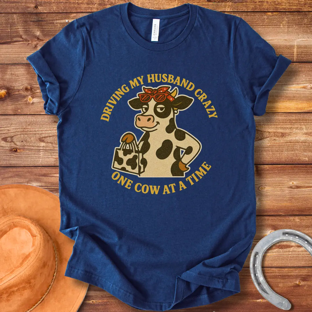 A cartoon cow wearing sunglasses and a bandana, holding a shopping bag, with the text 'Driving My Husband Crazy One Cow At A Time' around it.