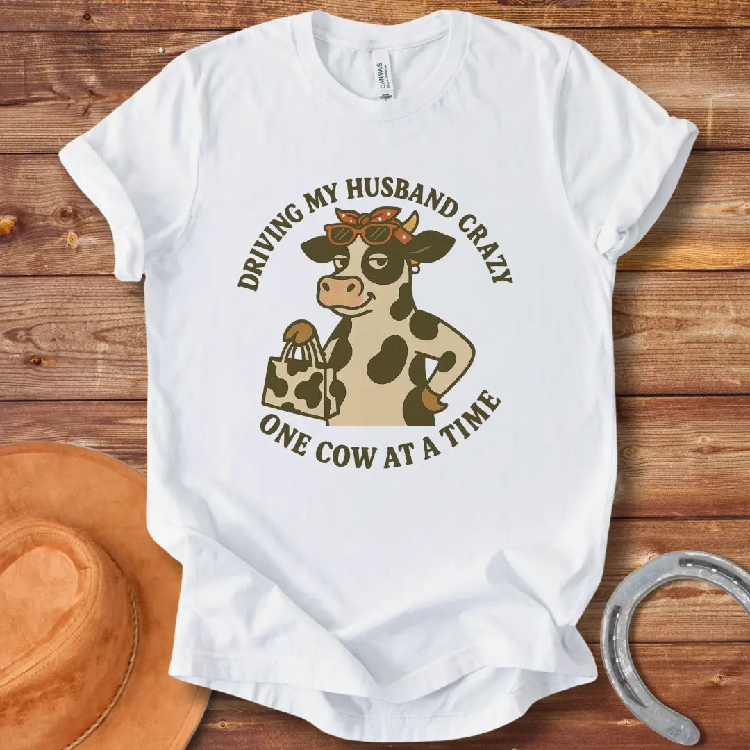 A cartoon cow wearing sunglasses and a bandana, holding a shopping bag, with the text 'Driving My Husband Crazy One Cow At A Time' around it.