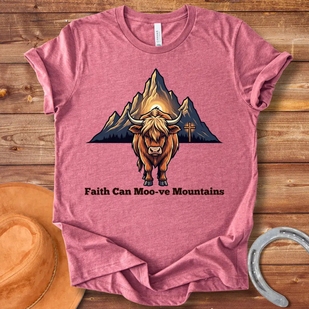 Highland cow graphic t-shirt with the words 'Faith Can Moo-ve Mountains', with mountain range and cross in the background