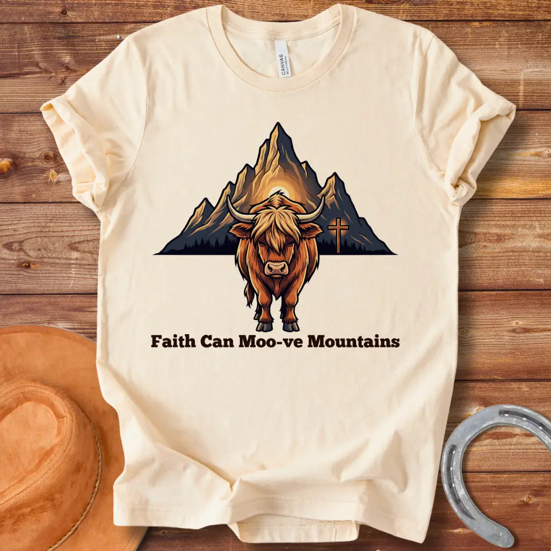 Highland cow graphic t-shirt with the words 'Faith Can Moo-ve Mountains', with mountain range and cross in the background