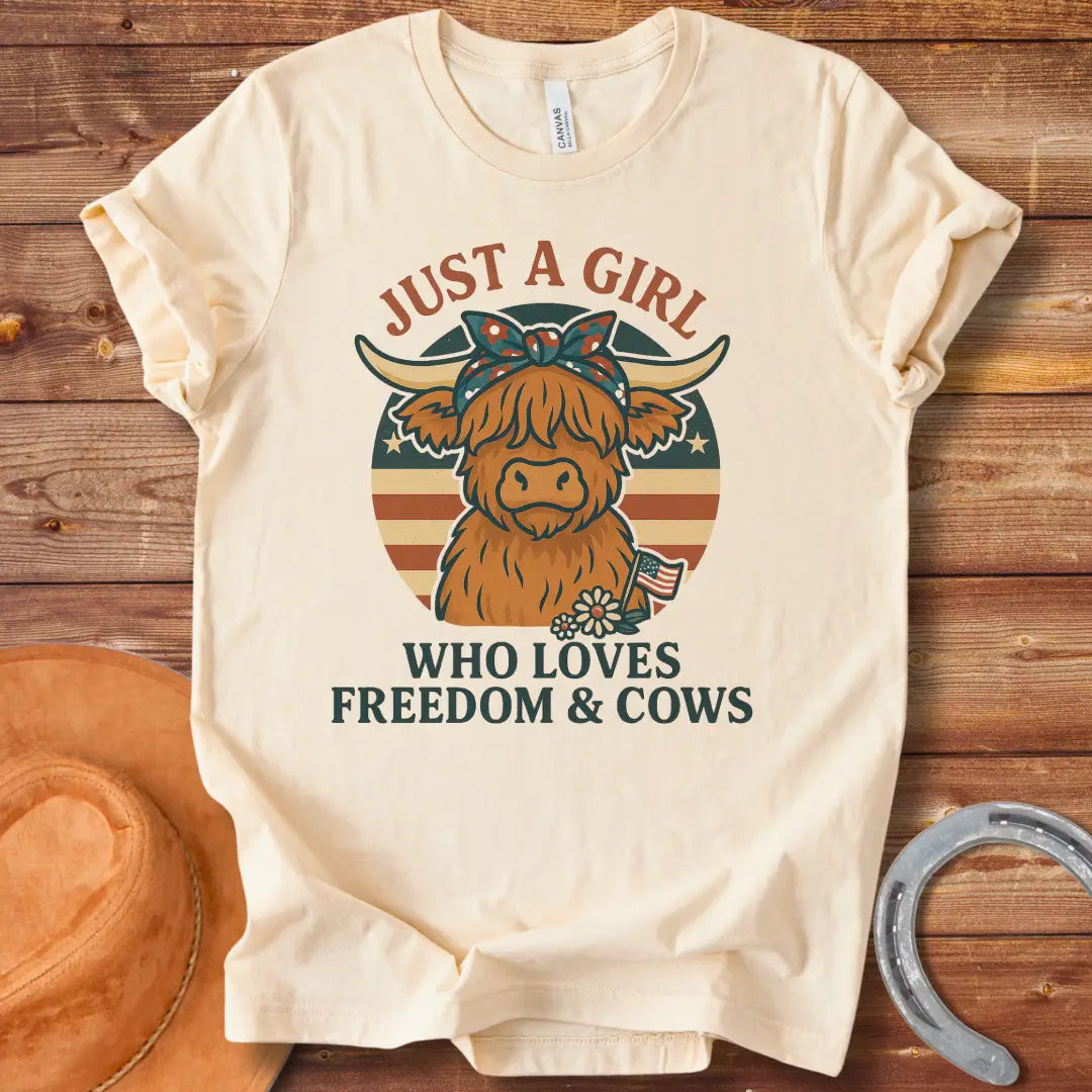 A cute Highland cow wearing a floral bandana, set against a patriotic American flag circle. Text reads 'Just a girl who loves freedom & cows'.