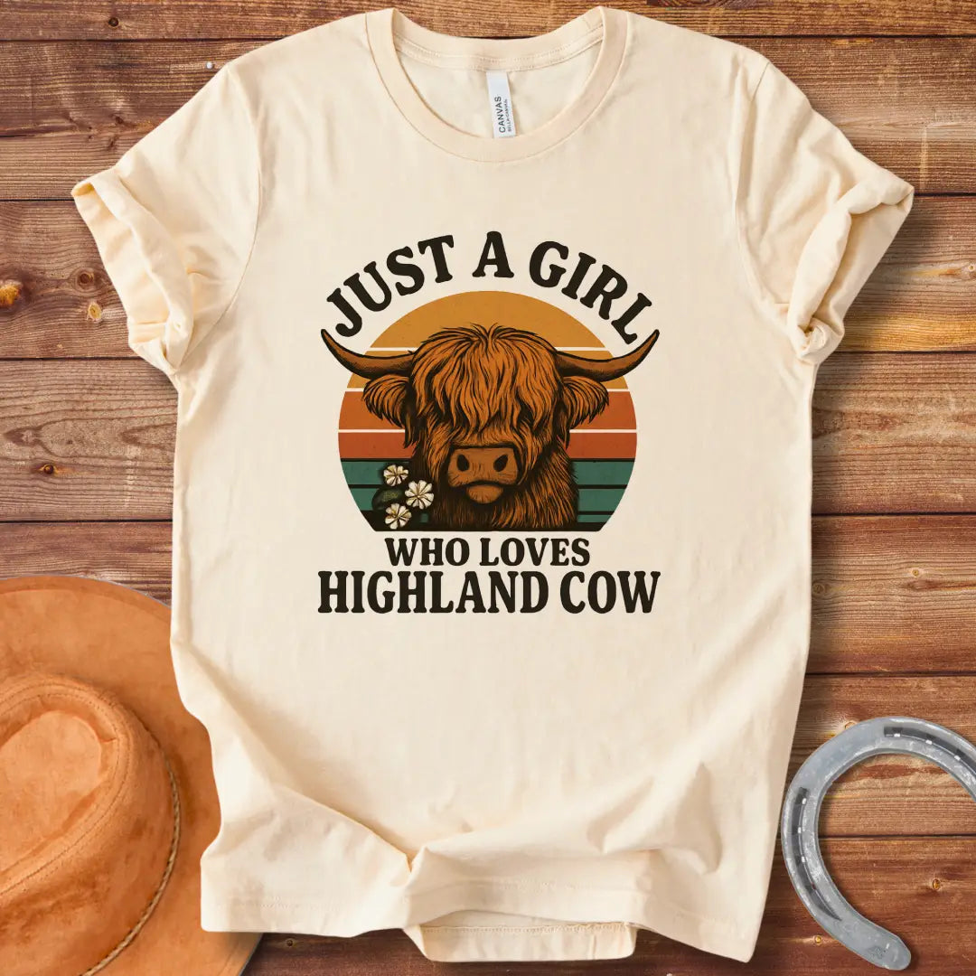 Vintage t-shirt featuring a Highland cow with flowers and the text 'Just a Girl Who Loves Highland Cow' against a retro sunset backdrop.