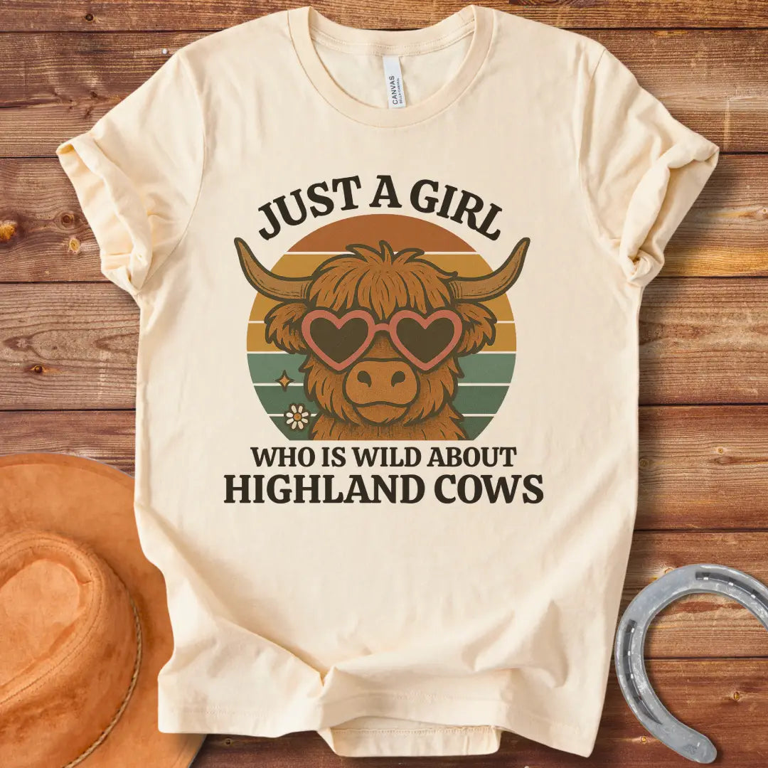 Girl Wild About Highland Cows t-shirt design featuring a Highland cow wearing heart-shaped sunglasses against a sunset backdrop.