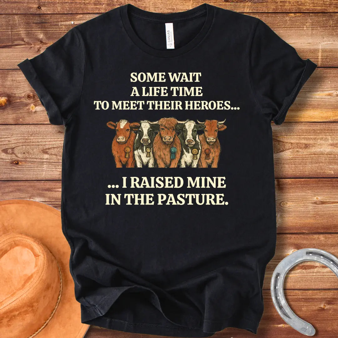 Heroes In The Pasture T-Shirt featuring five cows with ribbons, text saying 'Some wait a lifetime to meet their heroes... I raised mine in the pasture.'