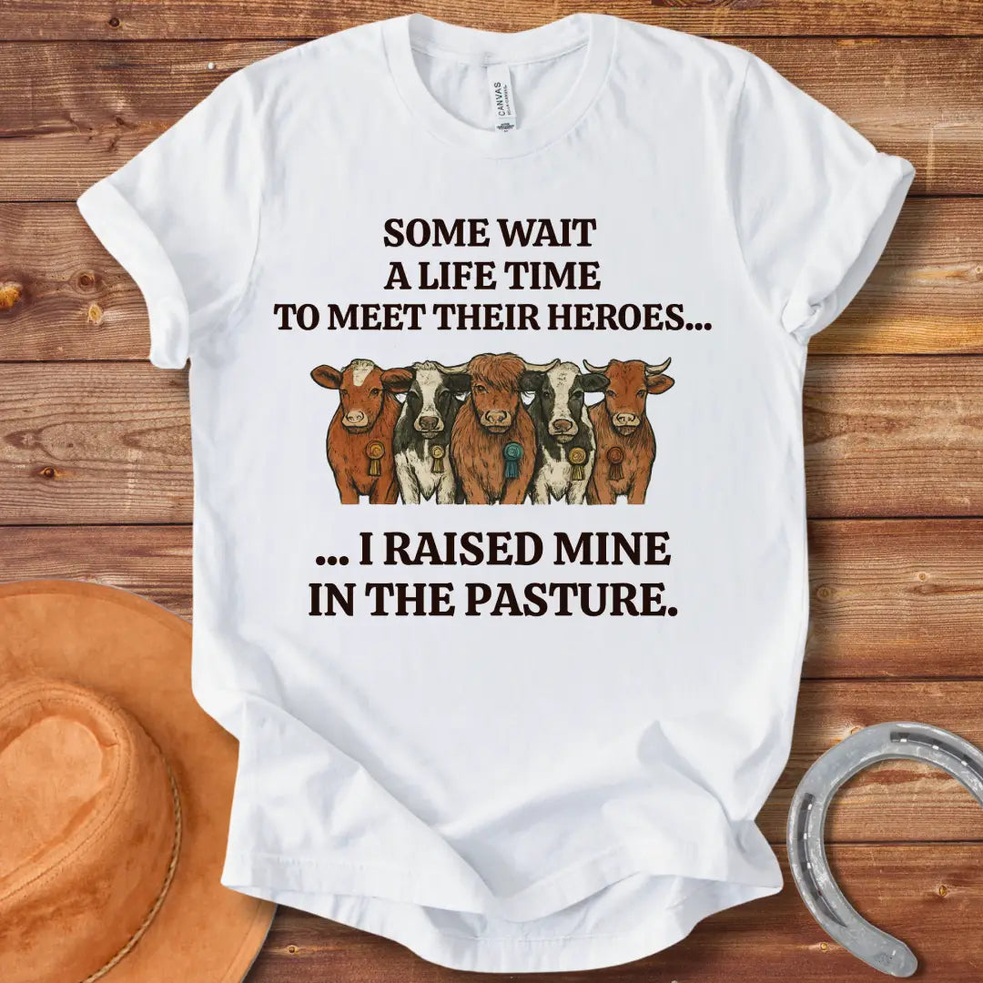 Heroes In The Pasture T-Shirt featuring five cows with ribbons, text saying 'Some wait a lifetime to meet their heroes... I raised mine in the pasture.'