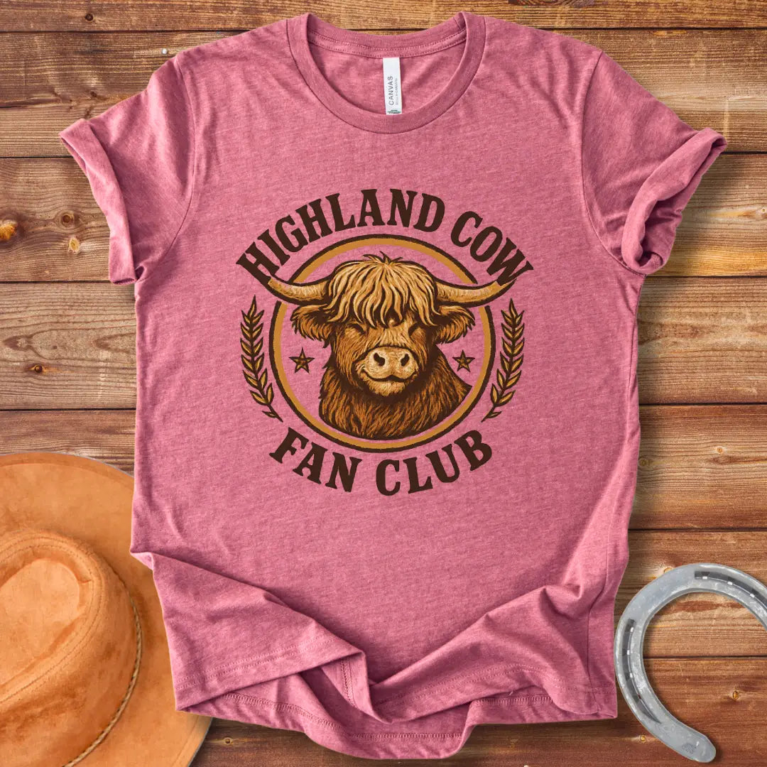 Highland Cow Fan Club T-Shirt featuring a smiling Highland cow in a circular design with text.
