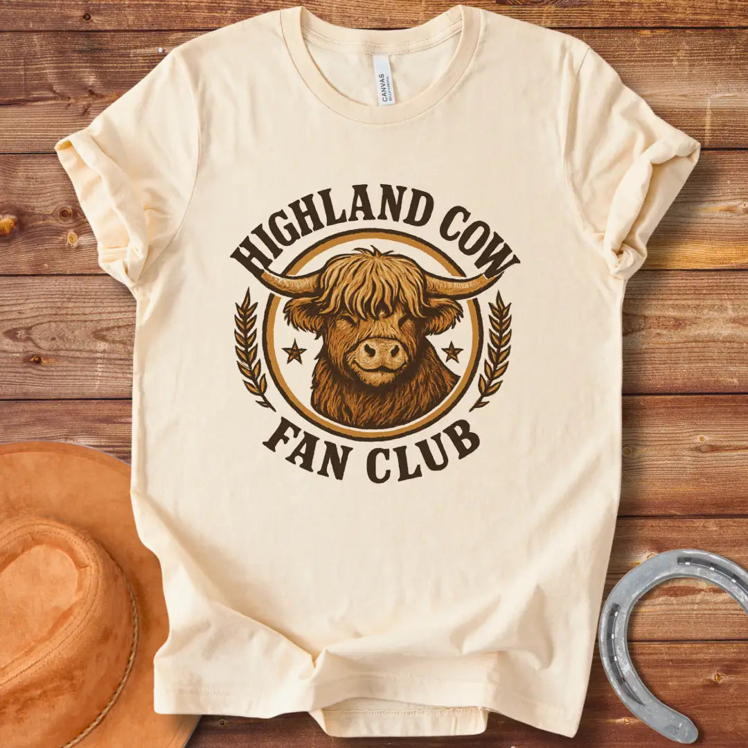 Highland Cow Fan Club T-Shirt featuring a smiling Highland cow in a circular design with text.