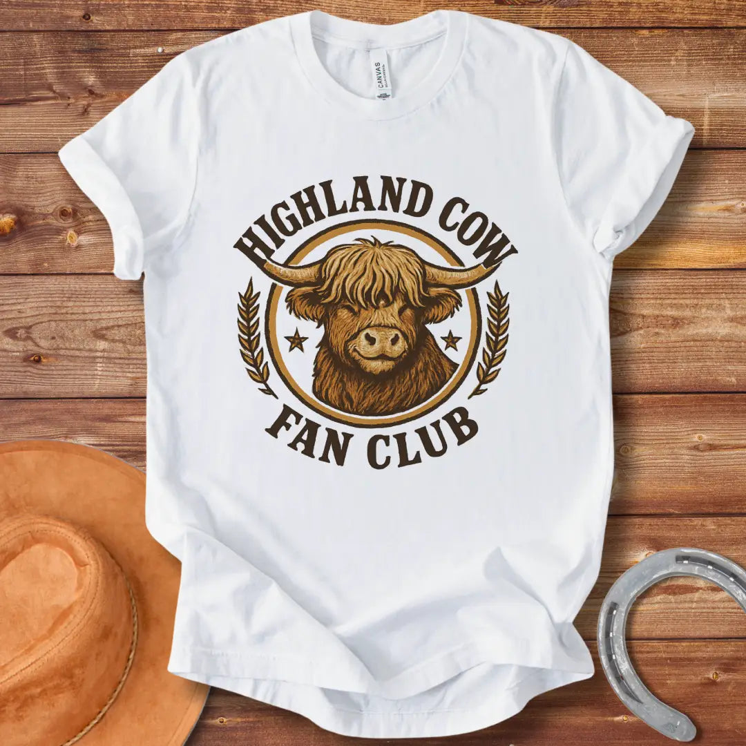 Highland Cow Fan Club T-Shirt featuring a smiling Highland cow in a circular design with text.