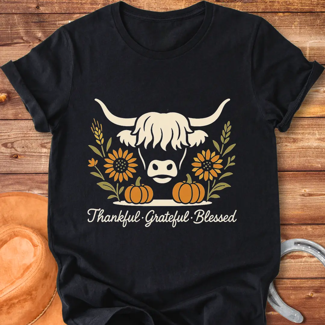 Highland cow with pumpkins, sunflower, and fall harvest design. Text reads: Thankful, Grateful, Blessed. Cow Lovers Clothing.