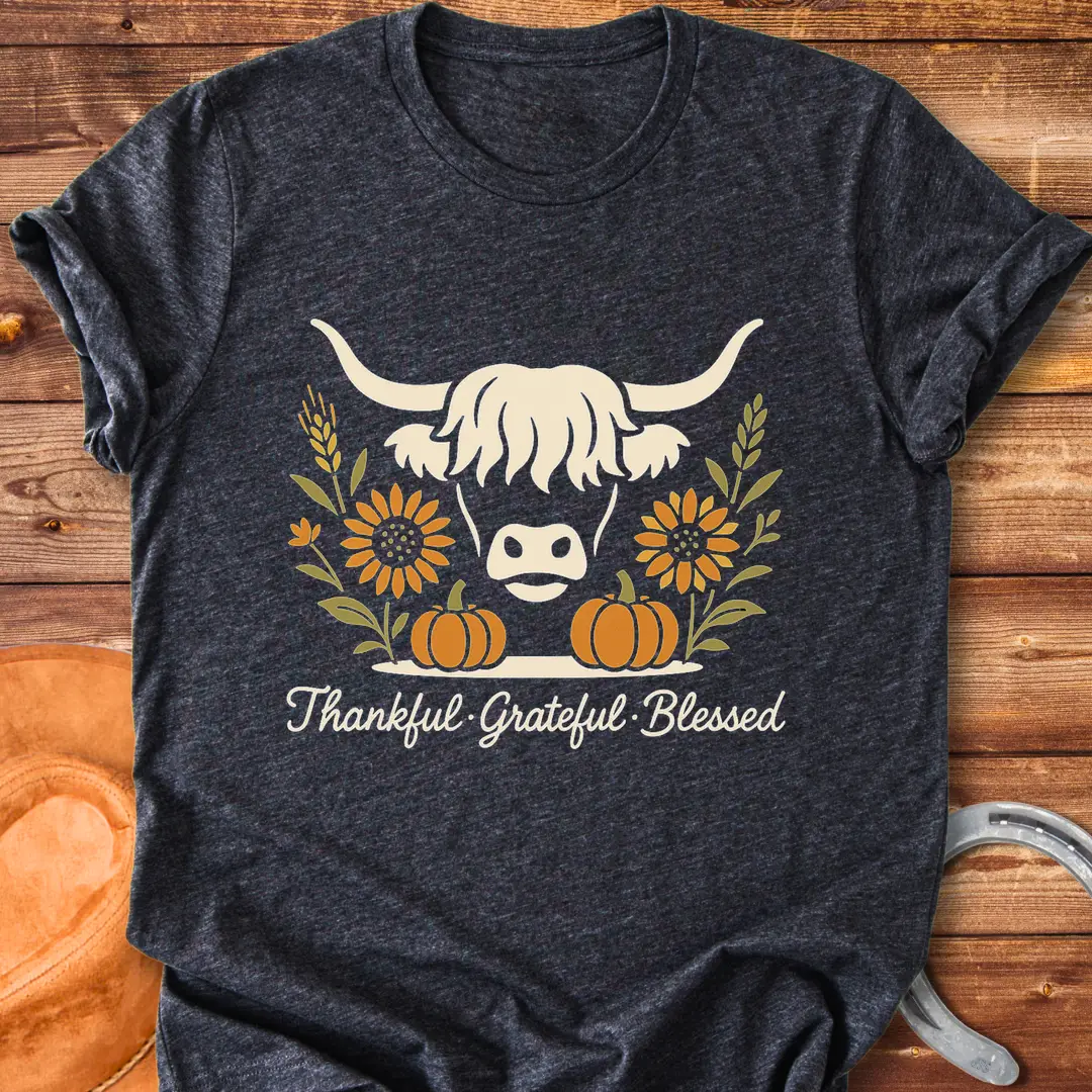 Highland cow with pumpkins, sunflower, and fall harvest design. Text reads: Thankful, Grateful, Blessed. Cow Lovers Clothing.