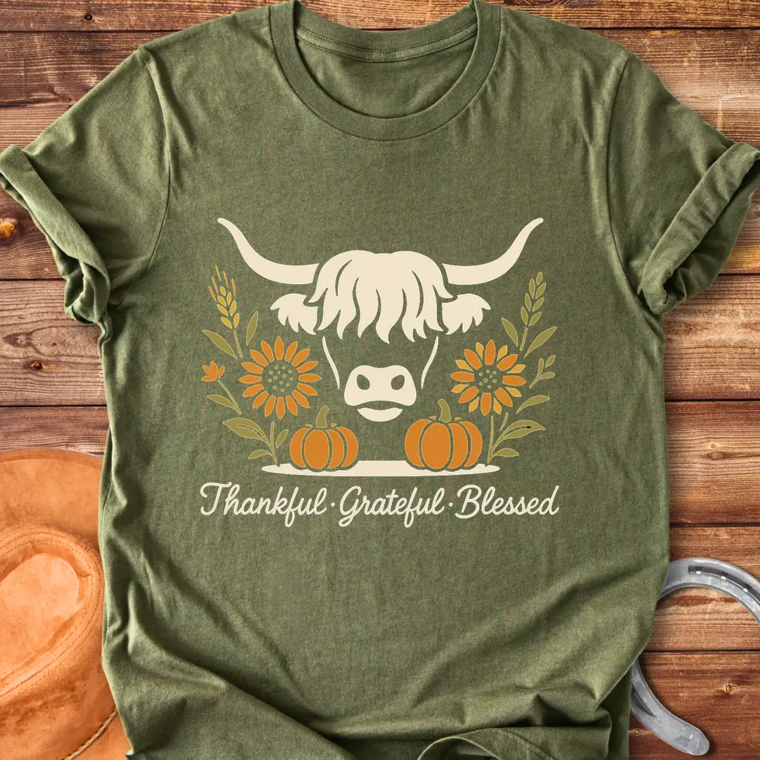 Highland cow with pumpkins, sunflower, and fall harvest design. Text reads: Thankful, Grateful, Blessed. Cow Lovers Clothing.