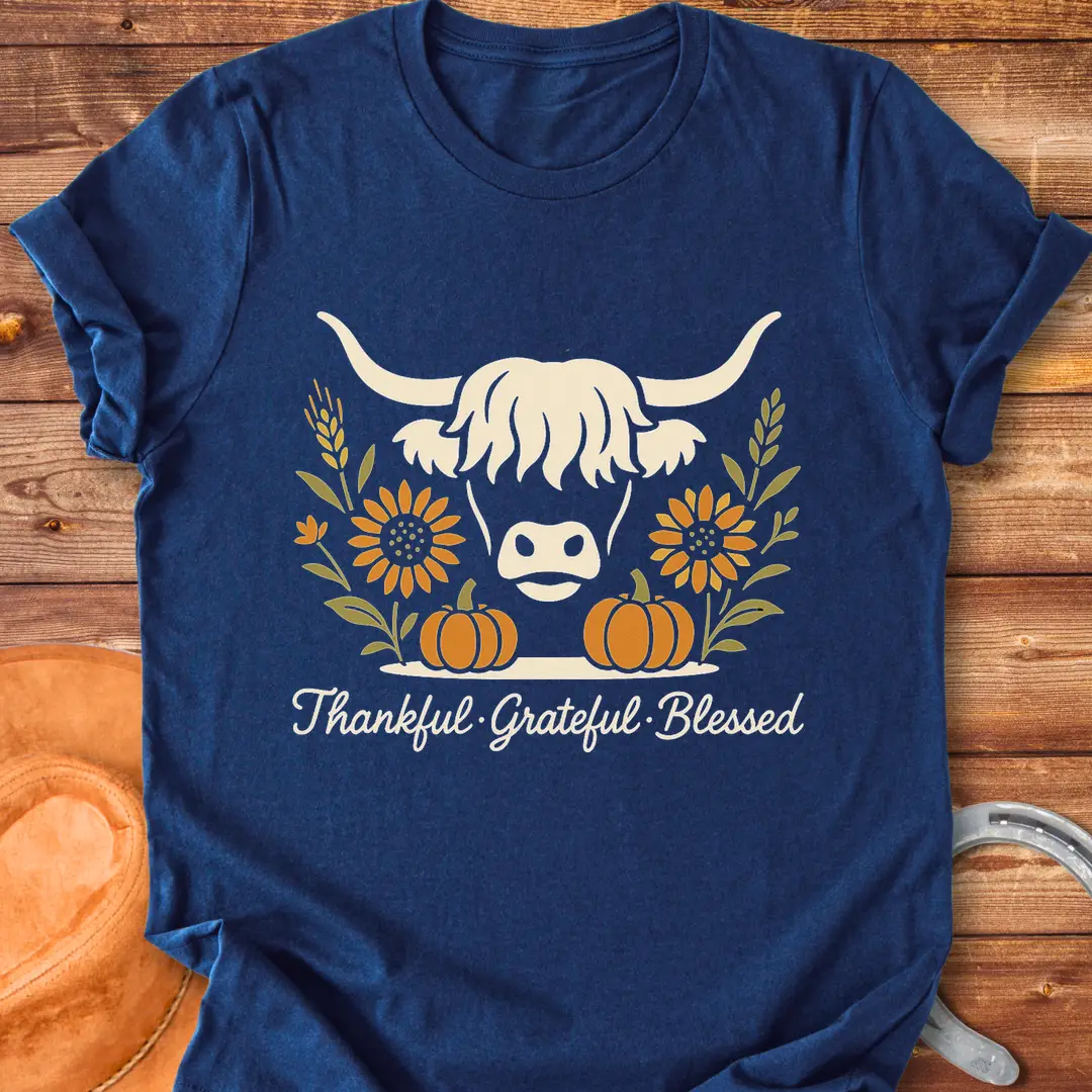 Highland cow with pumpkins, sunflower, and fall harvest design. Text reads: Thankful, Grateful, Blessed. Cow Lovers Clothing.