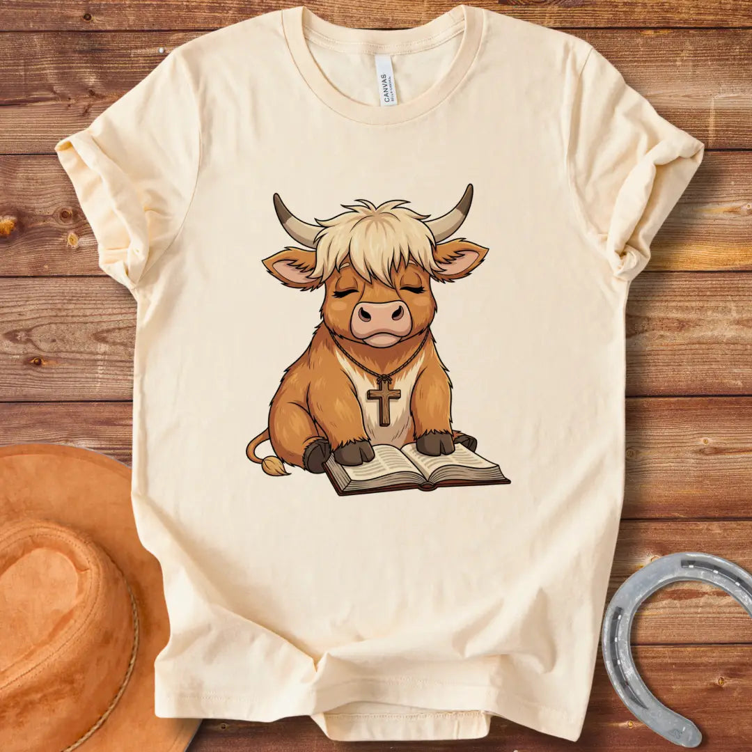 Cartoon illustration of a cow wearing a cross necklace, sitting peacefully with a book open in its lap.
