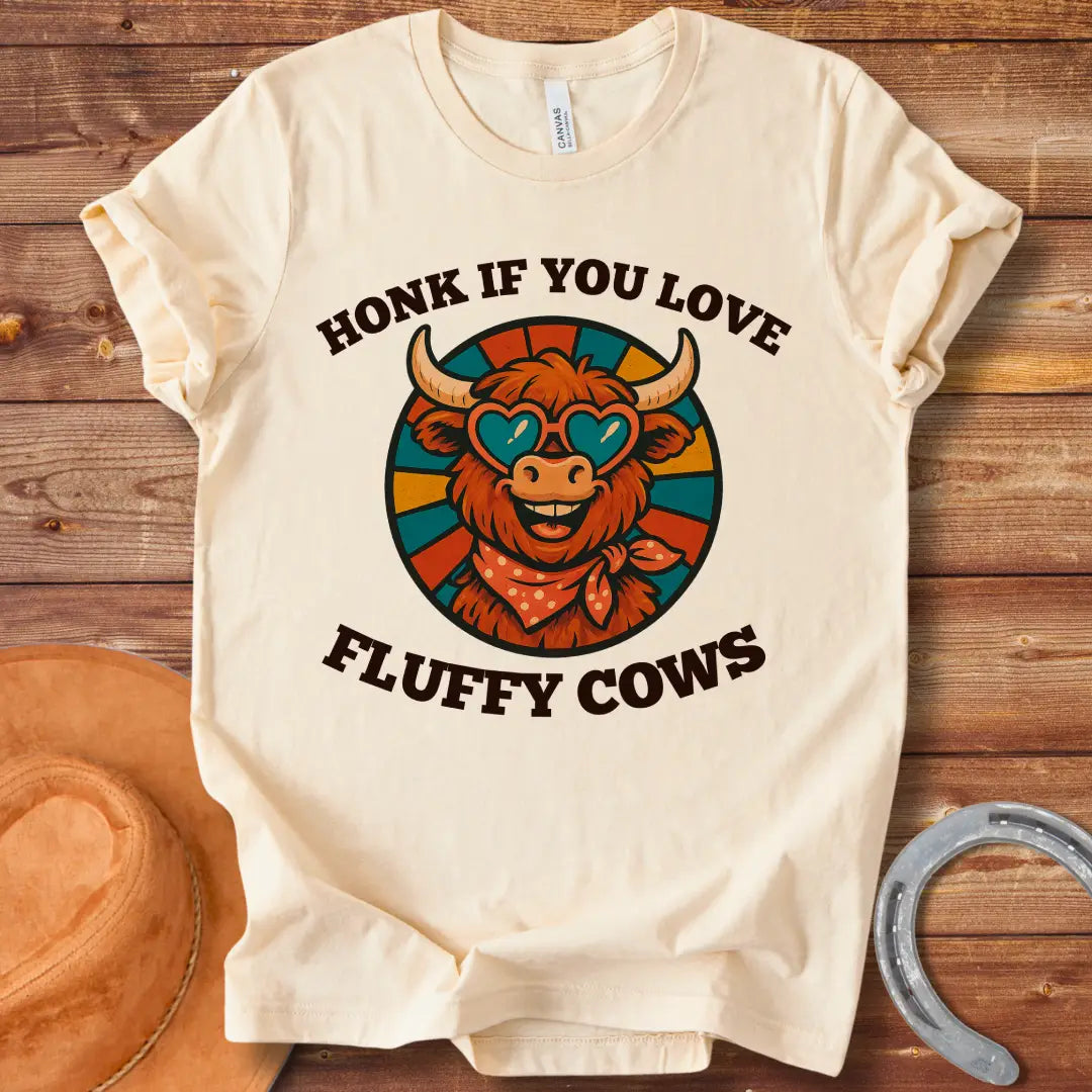 T-shirt design with a smiling cow wearing heart-shaped sunglasses and a bandana, with the text 'Honk If You Love Fluffy Cows'.