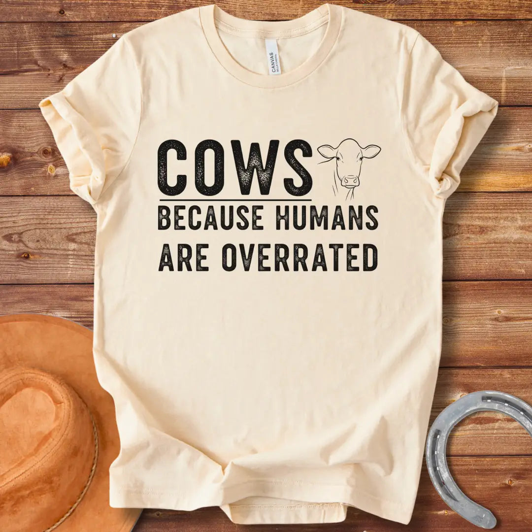 A black and white graphic t-shirt design that reads 'COWS BECAUSE HUMANS ARE OVERRATED' with a simple cow illustration.