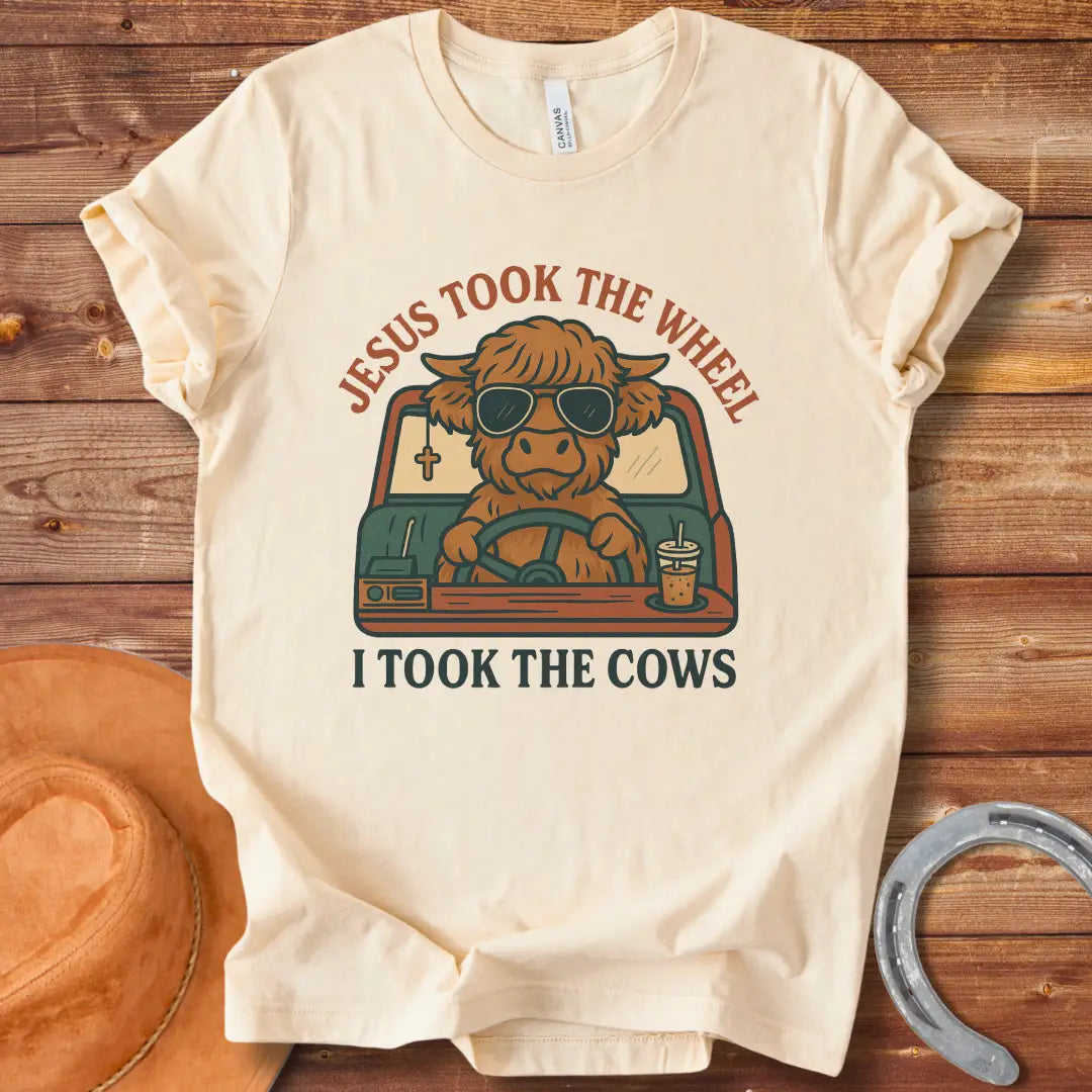 A Highland cow wearing sunglasses drives a car while holding a coffee; text reads 'Jesus took the wheel, I took the cows'.