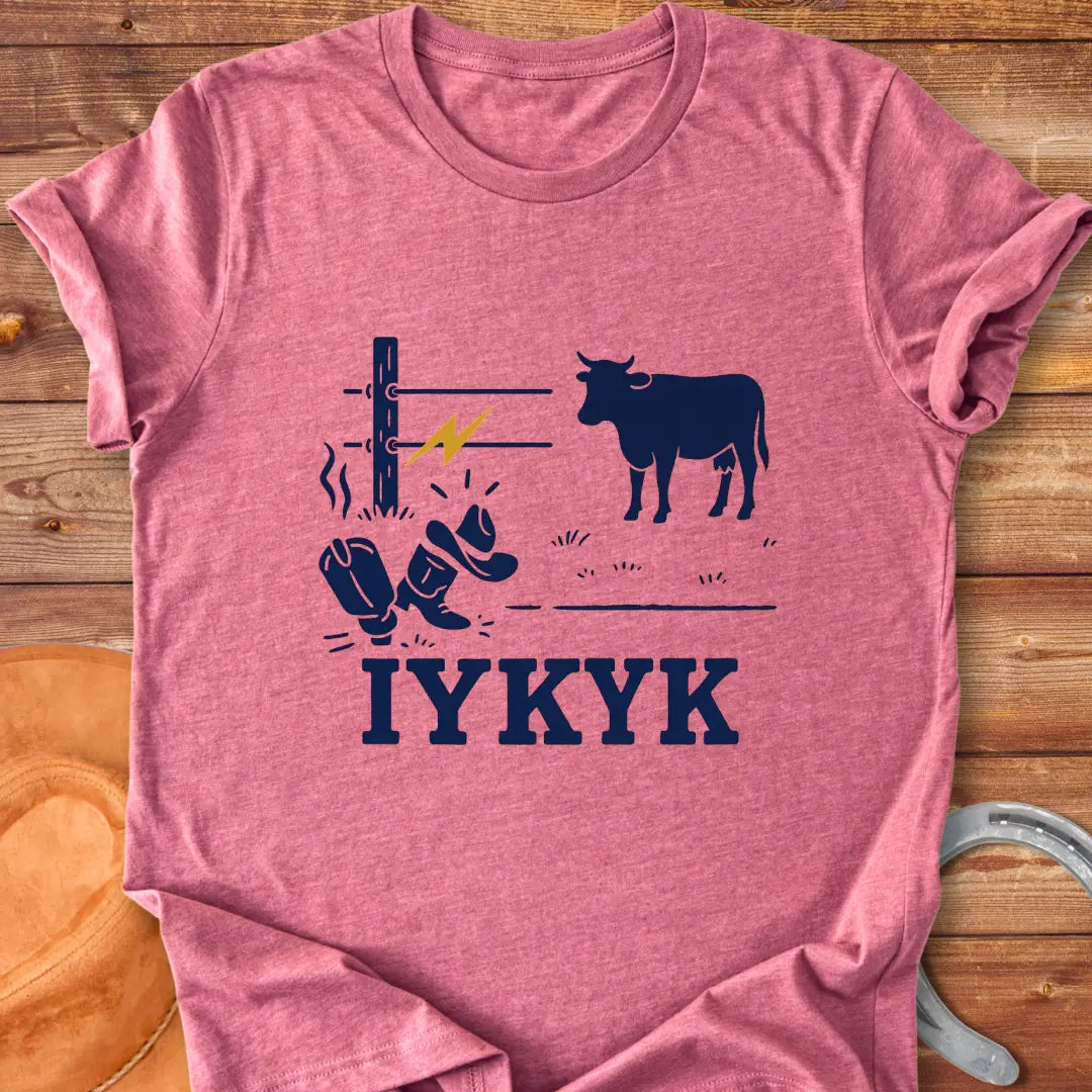 Graphic design on a t-shirt depicts a shocked cowboy hat and boots with a hot wire and a cow in the background, with the words IYKYK at the bottom