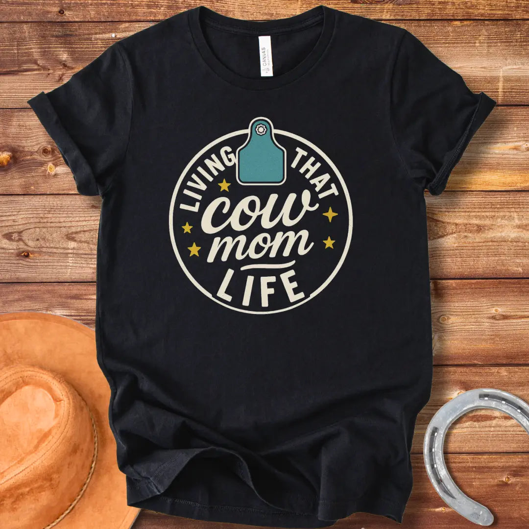 A round design featuring the text 'Living That Cow Mom Life' surrounding a cow tag graphic with orange stars.