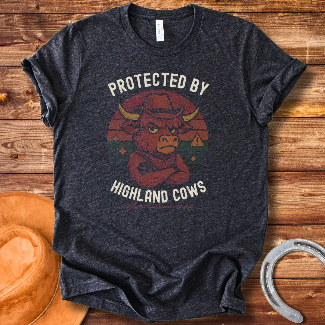 Protected by Highland Cows t-shirt featuring a cartoon Highland cow wearing a cowboy hat with a stern look.