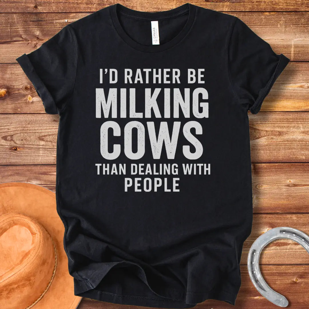 A black and white graphic t-shirt design with the text 'I'd rather be milking cows than dealing with people'.