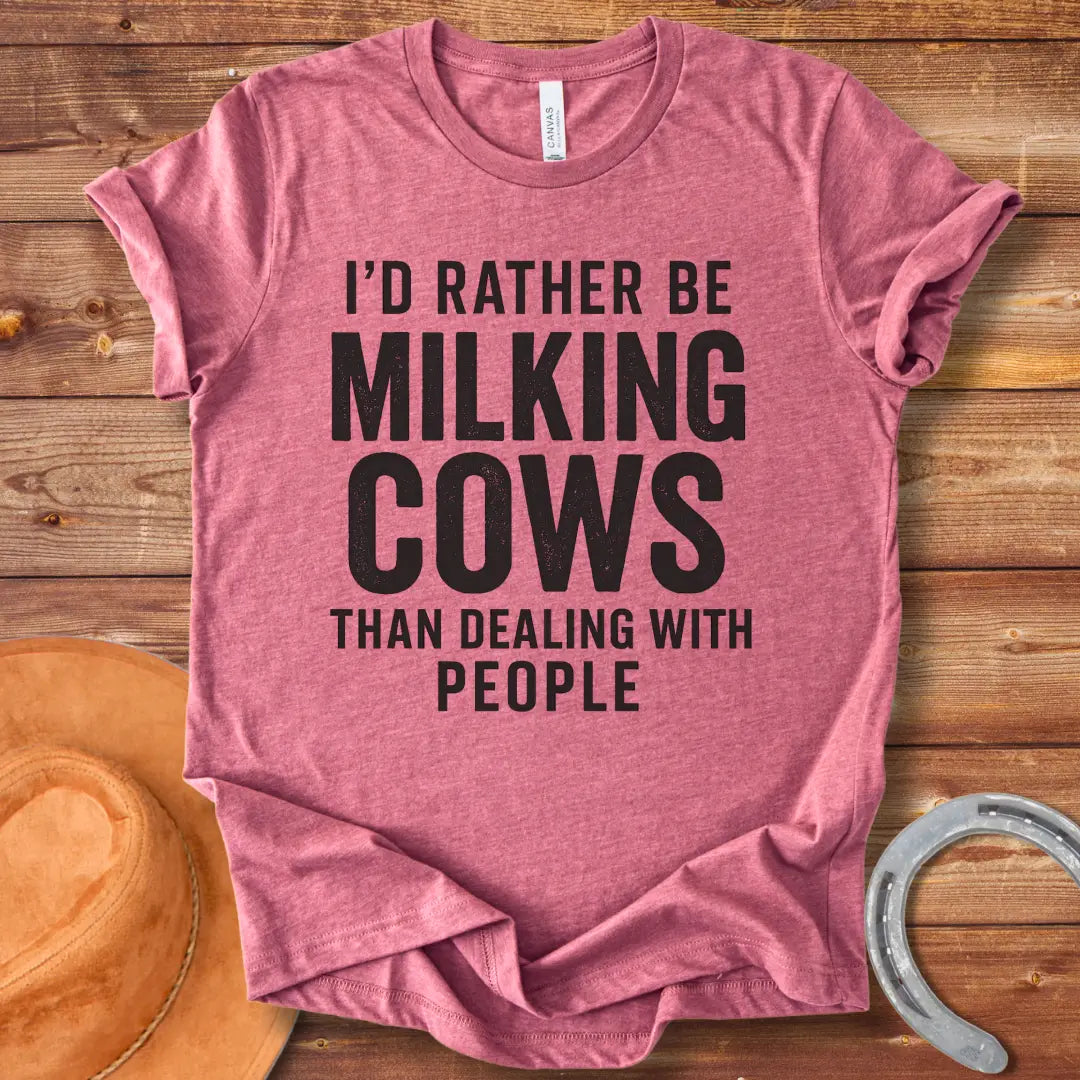 A black and white graphic t-shirt design with the text 'I'd rather be milking cows than dealing with people'.