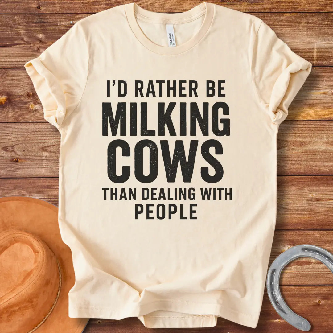 A black and white graphic t-shirt design with the text 'I'd rather be milking cows than dealing with people'.