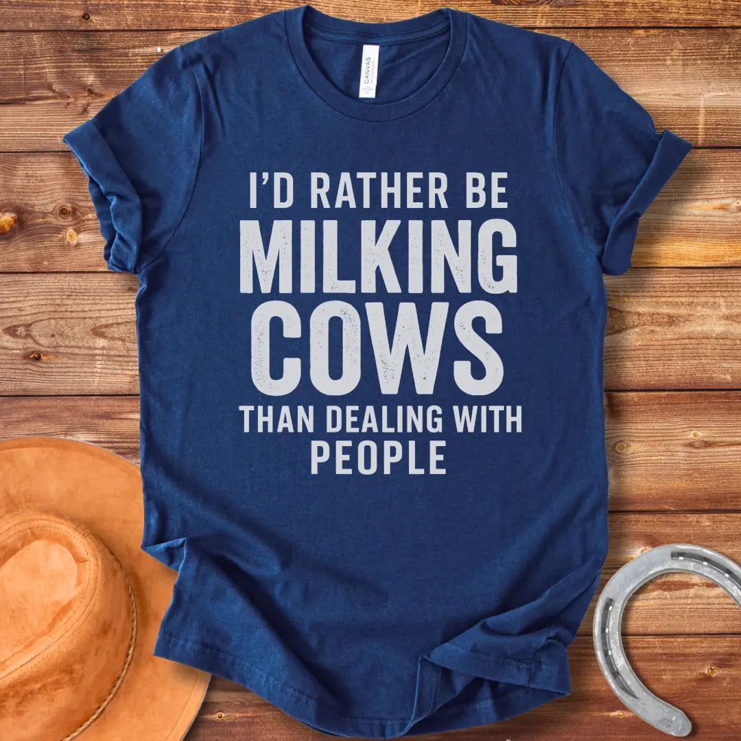 A black and white graphic t-shirt design with the text 'I'd rather be milking cows than dealing with people'.