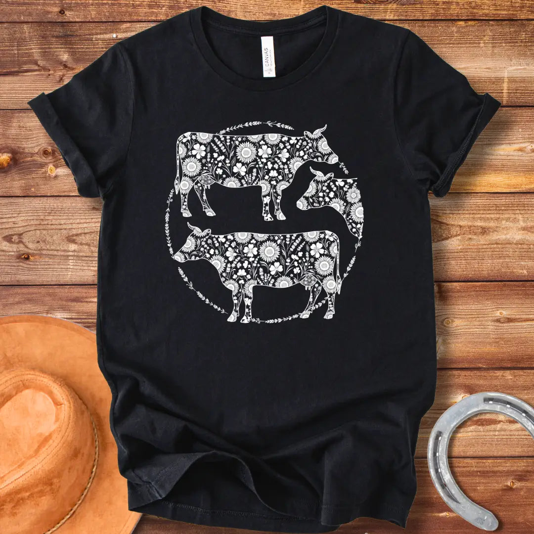 Black and white illustration of three cows with floral patterns within a circle.