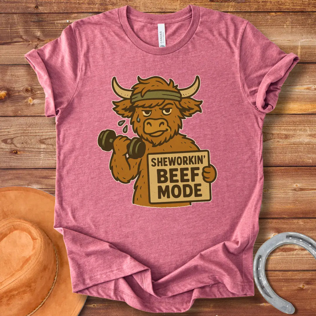 Cartoon cow working out with dumbbells, wearing a headband and holding a sign that says 'Sheworkin' Beef Mode'
