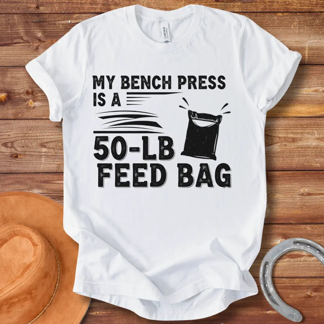 A graphic design on a t-shirt showing a humorous depiction of a feed bag labeled as a '50-lb' weight for a bench press.