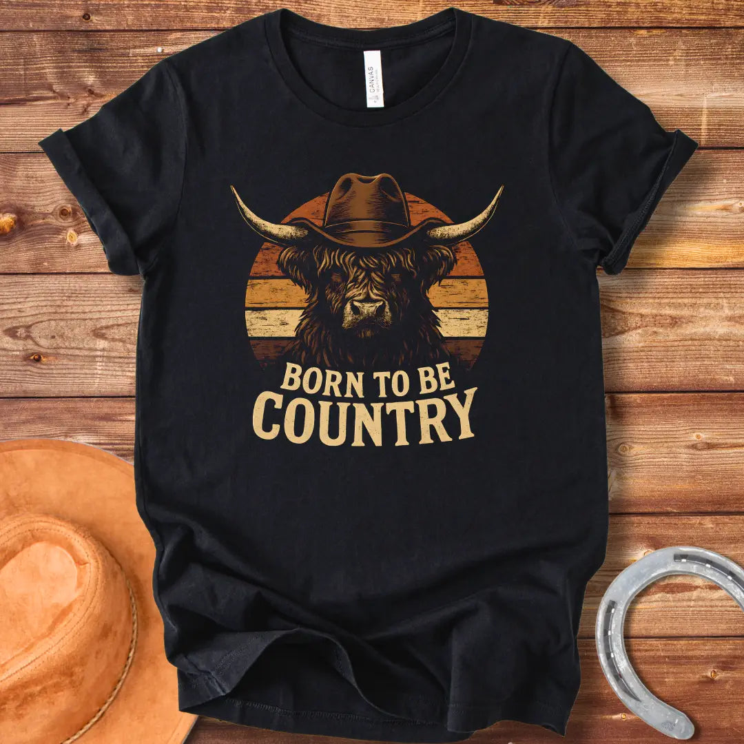 Born To Be Country T-shirt featuring a Highland cow wearing a cowboy hat against a sunset backdrop. Perfect for cow lovers.