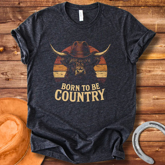 Born To Be Country T-shirt featuring a Highland cow wearing a cowboy hat against a sunset backdrop. Perfect for cow lovers.
