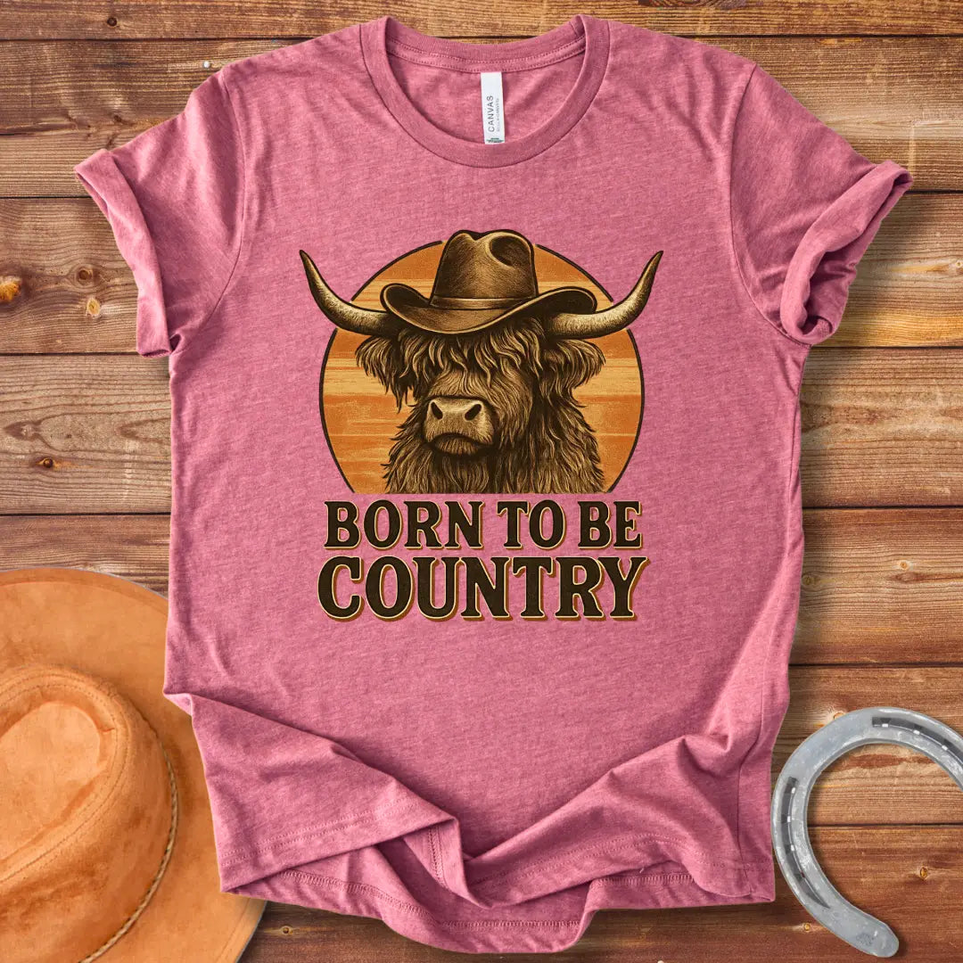 Born To Be Country T-shirt featuring a Highland cow wearing a cowboy hat against a sunset backdrop. Perfect for cow lovers.