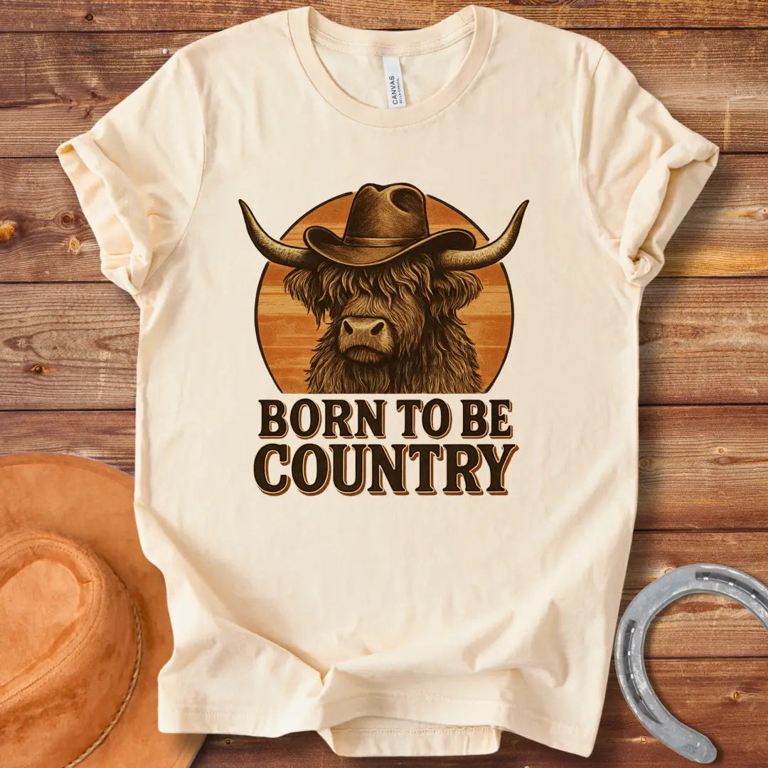 Born To Be Country T-shirt featuring a Highland cow wearing a cowboy hat against a sunset backdrop. Perfect for cow lovers.
