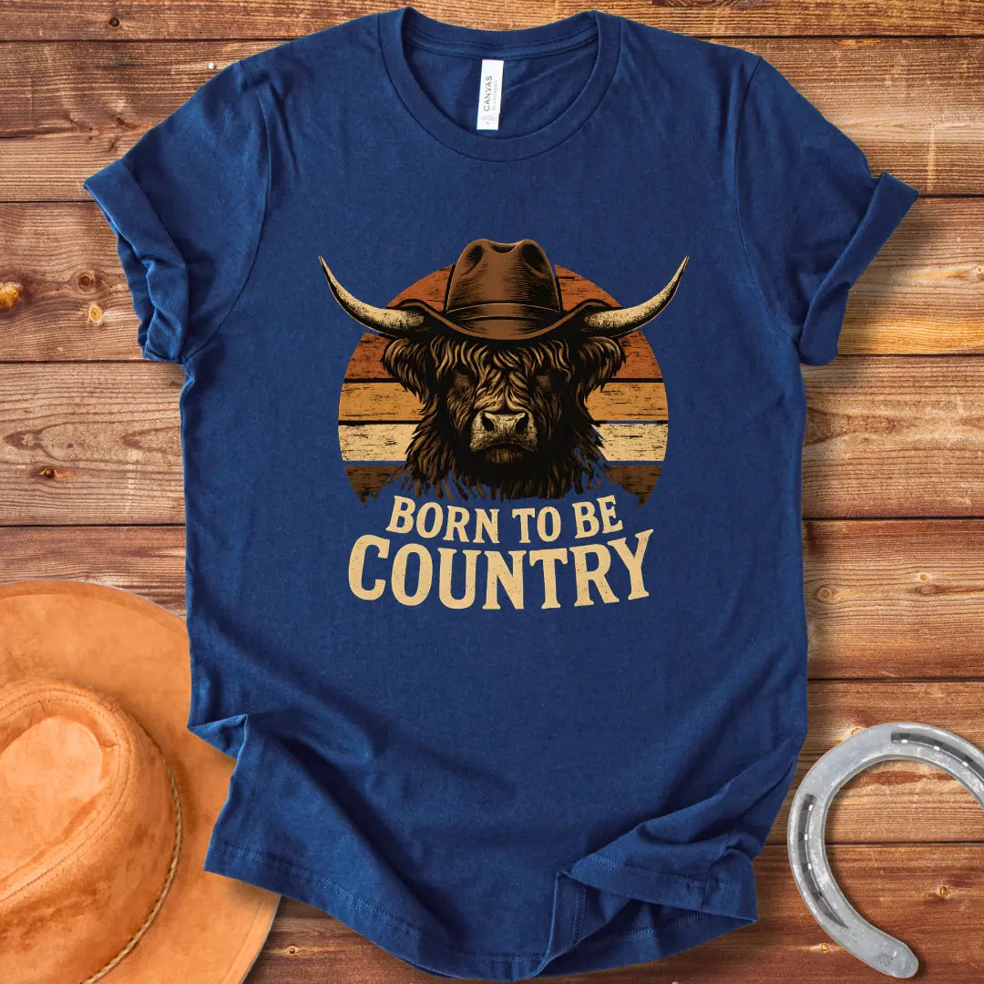 Born To Be Country T-shirt featuring a Highland cow wearing a cowboy hat against a sunset backdrop. Perfect for cow lovers.