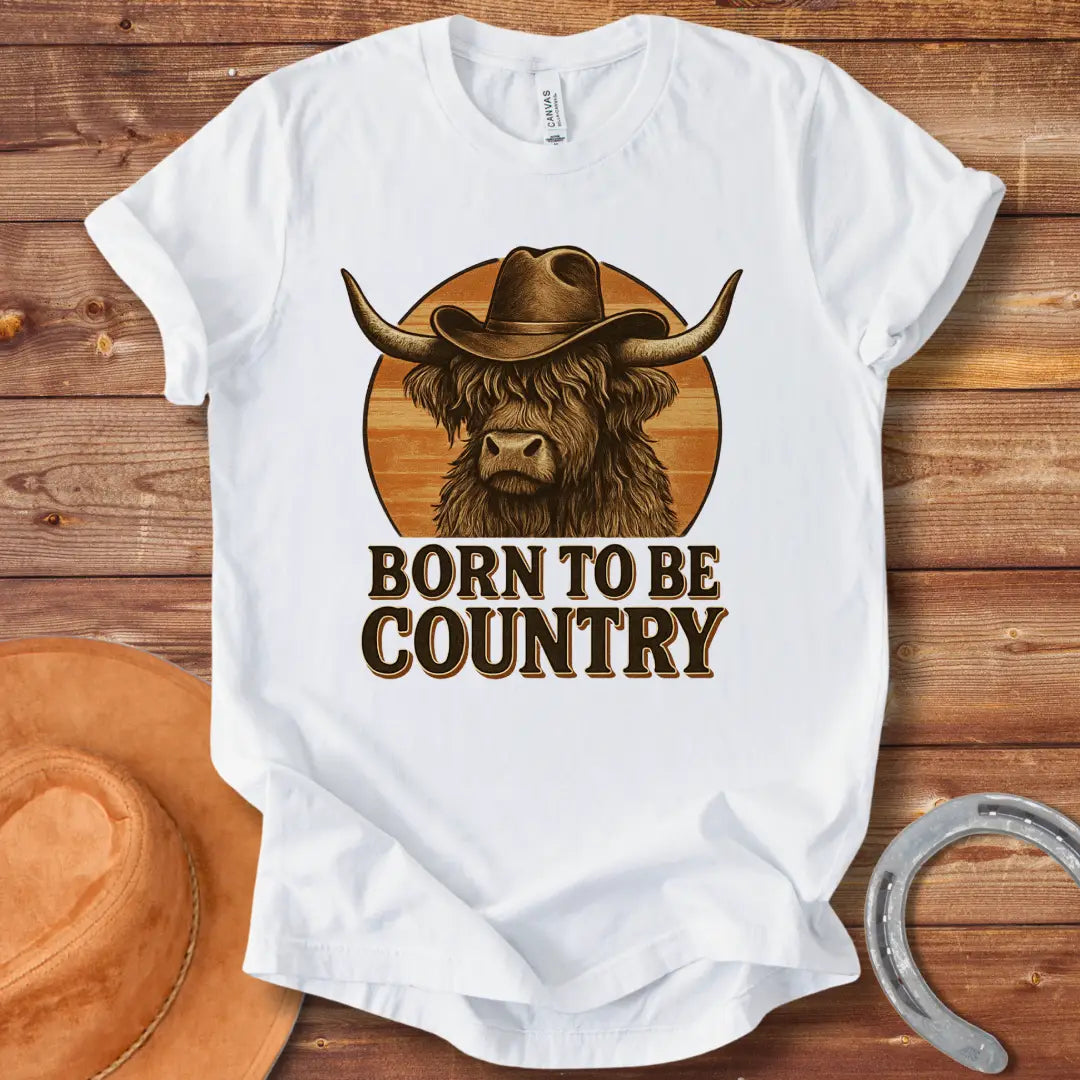 Born To Be Country T-shirt featuring a Highland cow wearing a cowboy hat against a sunset backdrop. Perfect for cow lovers.