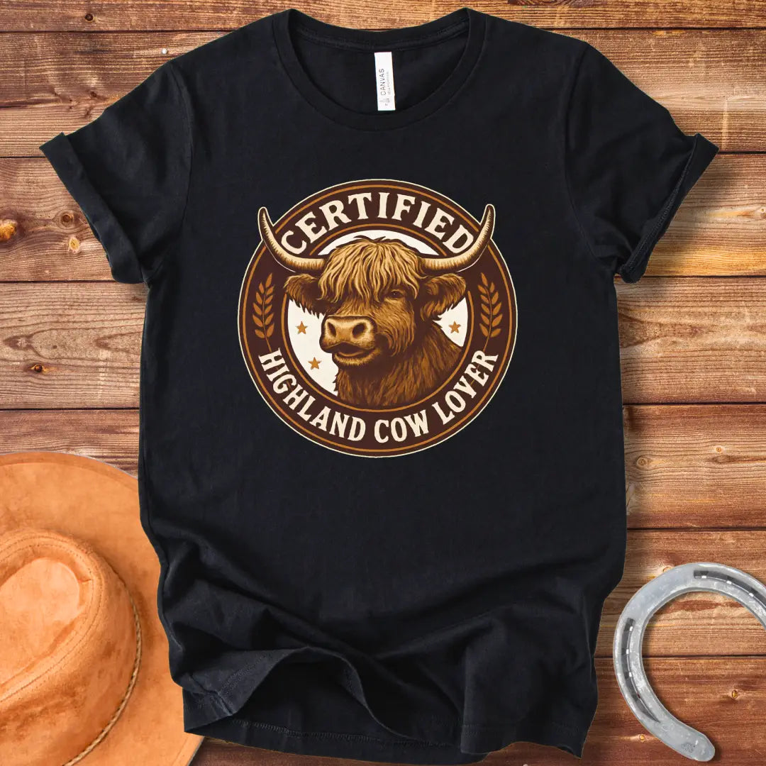 Certified Highland Cow Lover T-Shirt graphic featuring a detailed illustration of a Highland cow's head inside a circular badge.