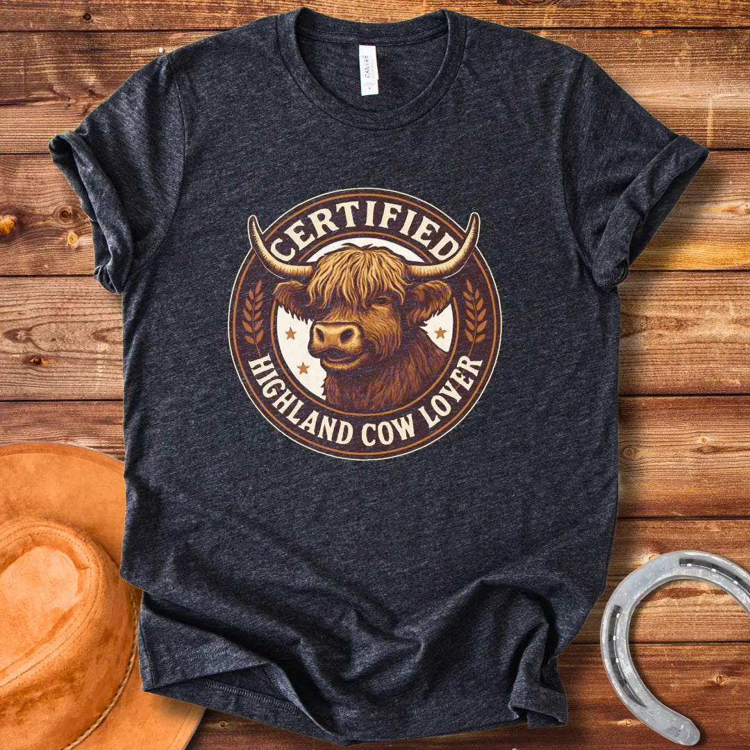 Certified Highland Cow Lover T-Shirt graphic featuring a detailed illustration of a Highland cow's head inside a circular badge.